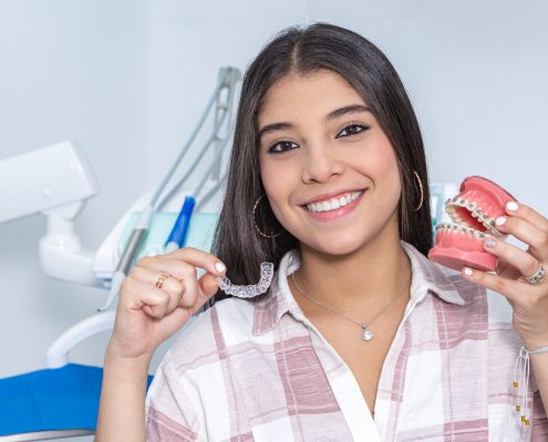 Cheerful ethnic teen girl showing denture and retainer in dental clinic
